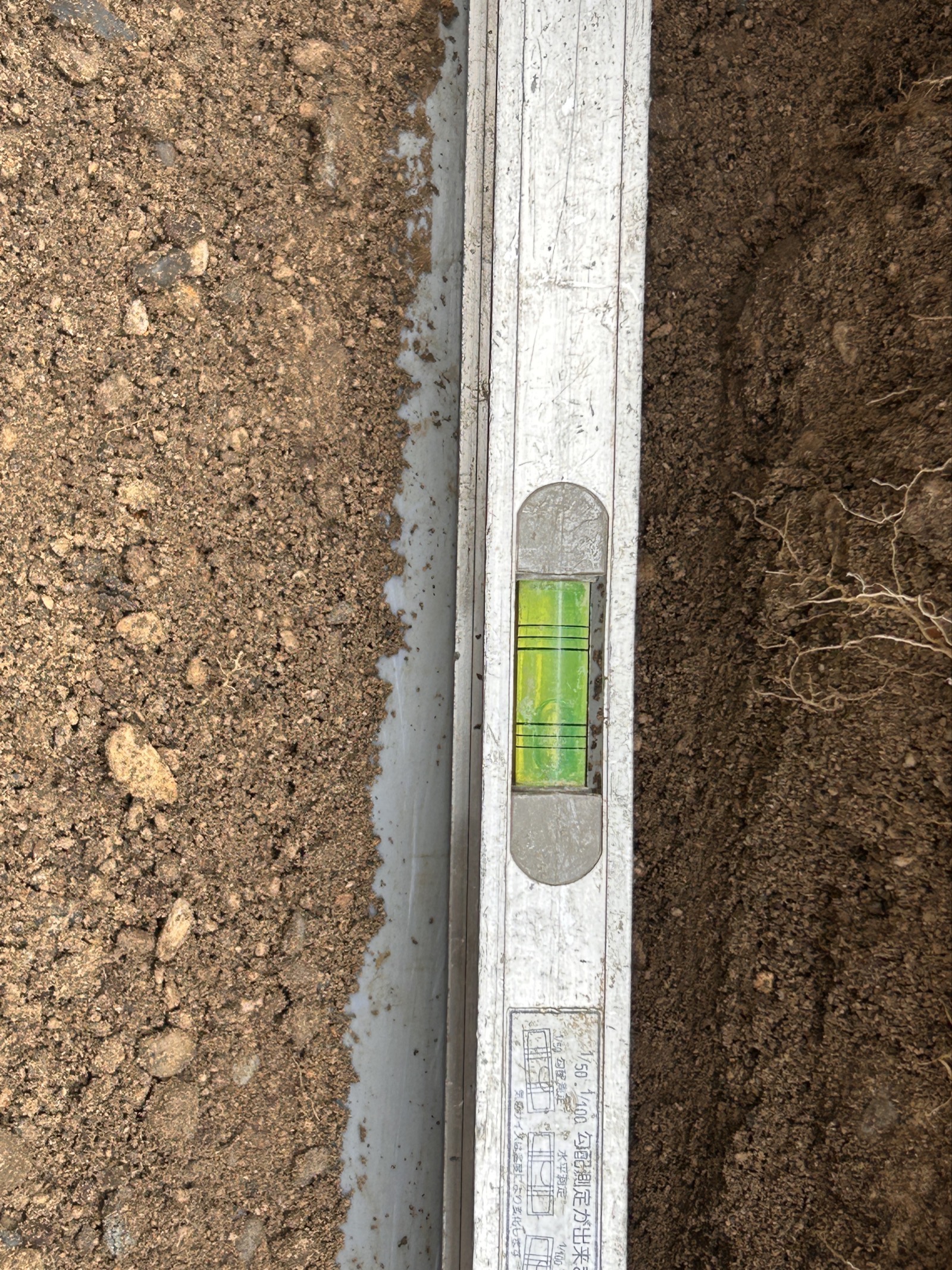 勾配確認：新しい塩ビ管に水平器を当てて勾配を厳密に確認している