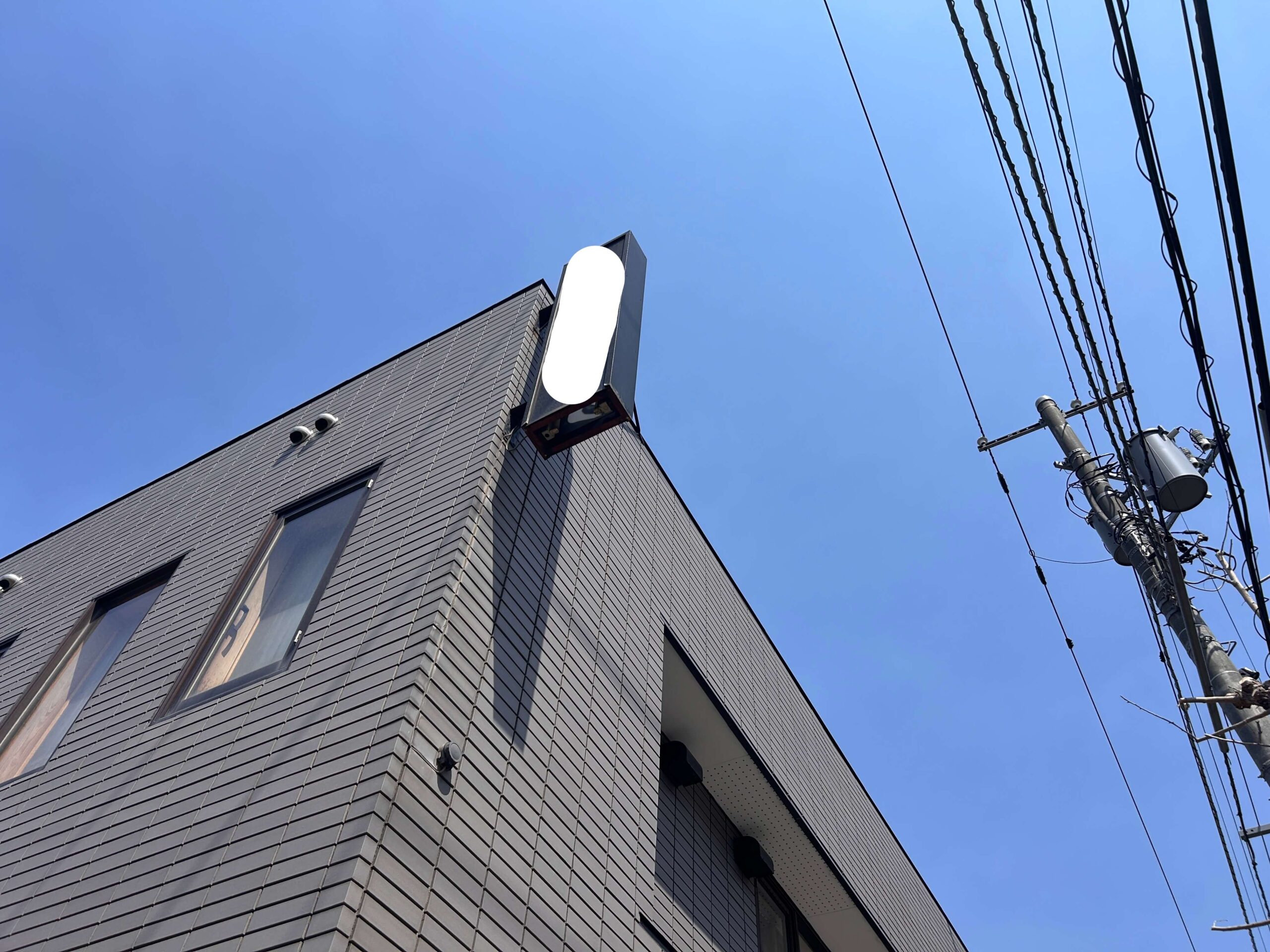 施工前：別角度から見た看板の取付状況。建物コーナーに縦長の袖看板が設置されており、高さがある。