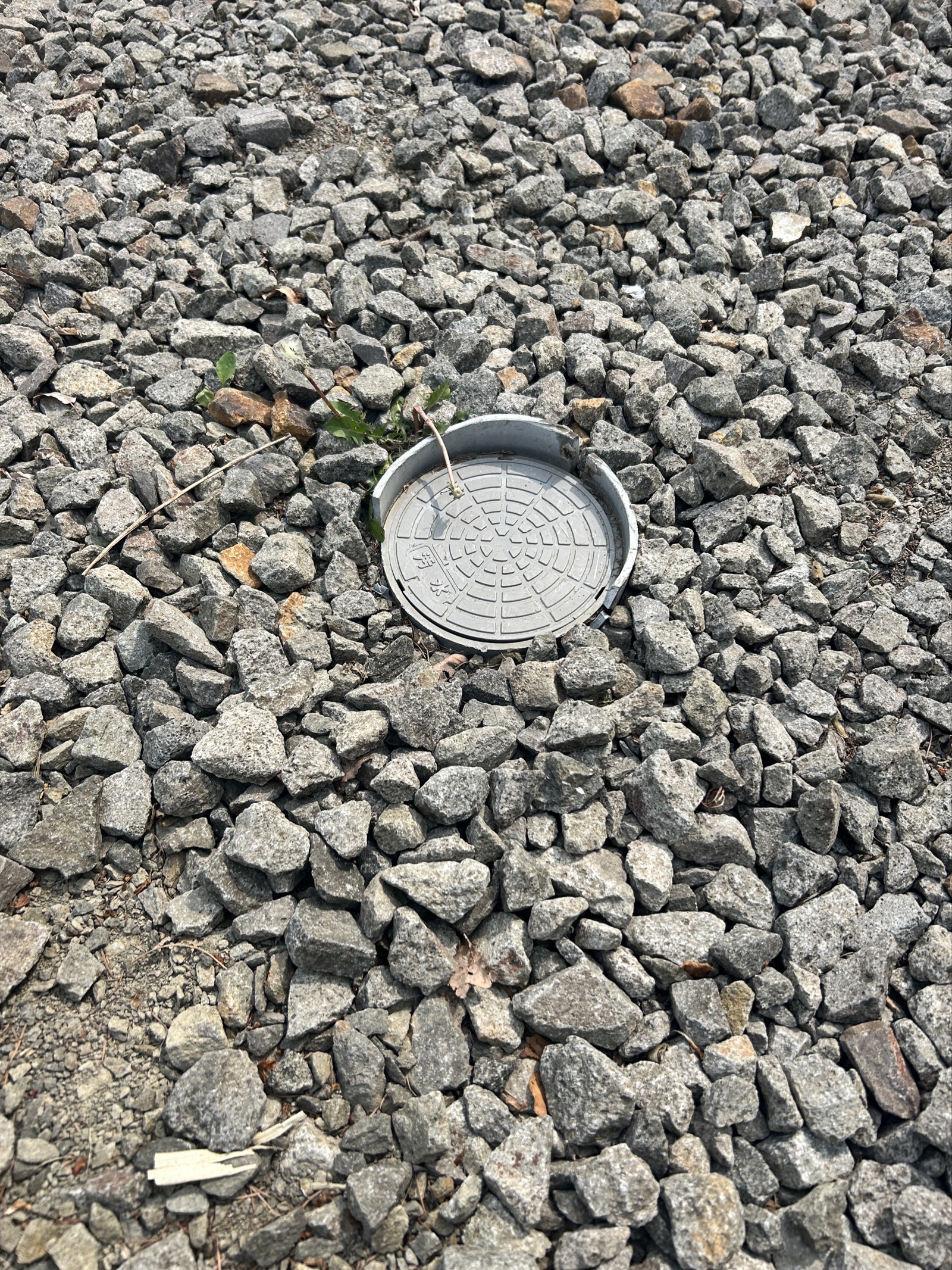 着工前:砕石敷き駐車スペースに埋まった排水マス。地表から見ると蓋のみが確認できる状態