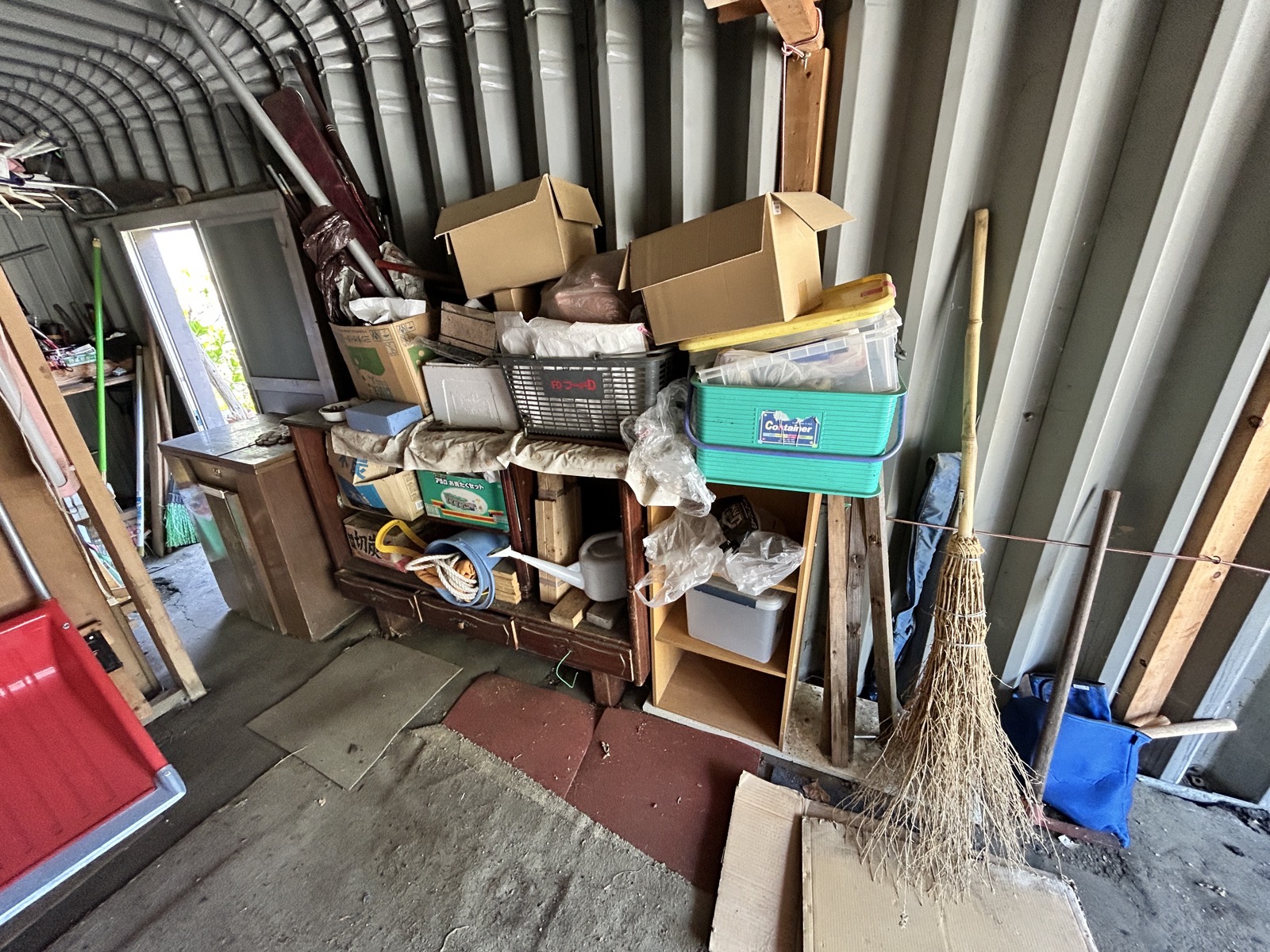 施工前・車庫内部。農具・スコップ・コンテナ・塗料缶など立体的に積み上がった状態