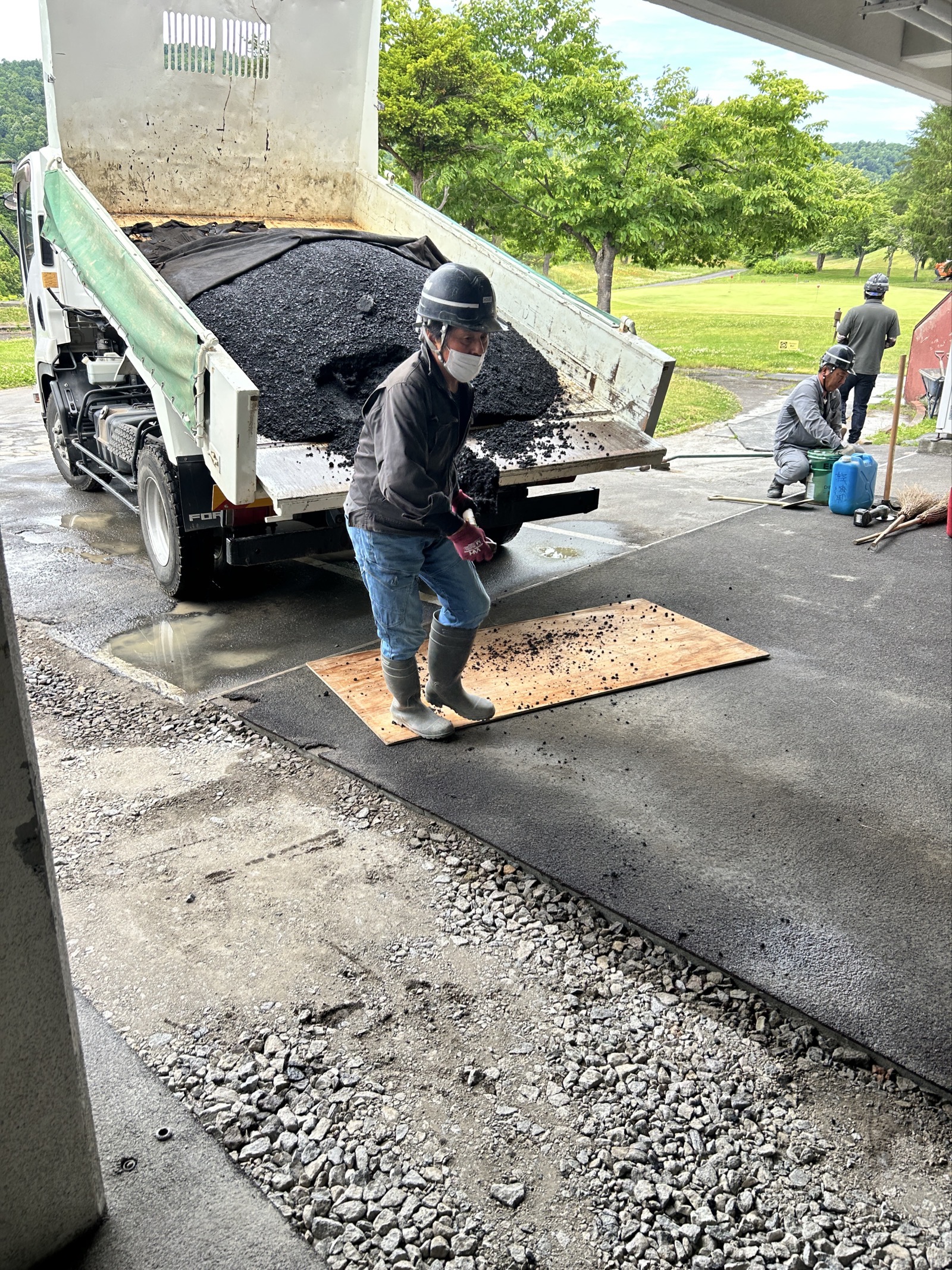 ダンプから加熱アスファルト合材を荷下ろしする様子。搬入後は素早く敷均し・転圧に移る