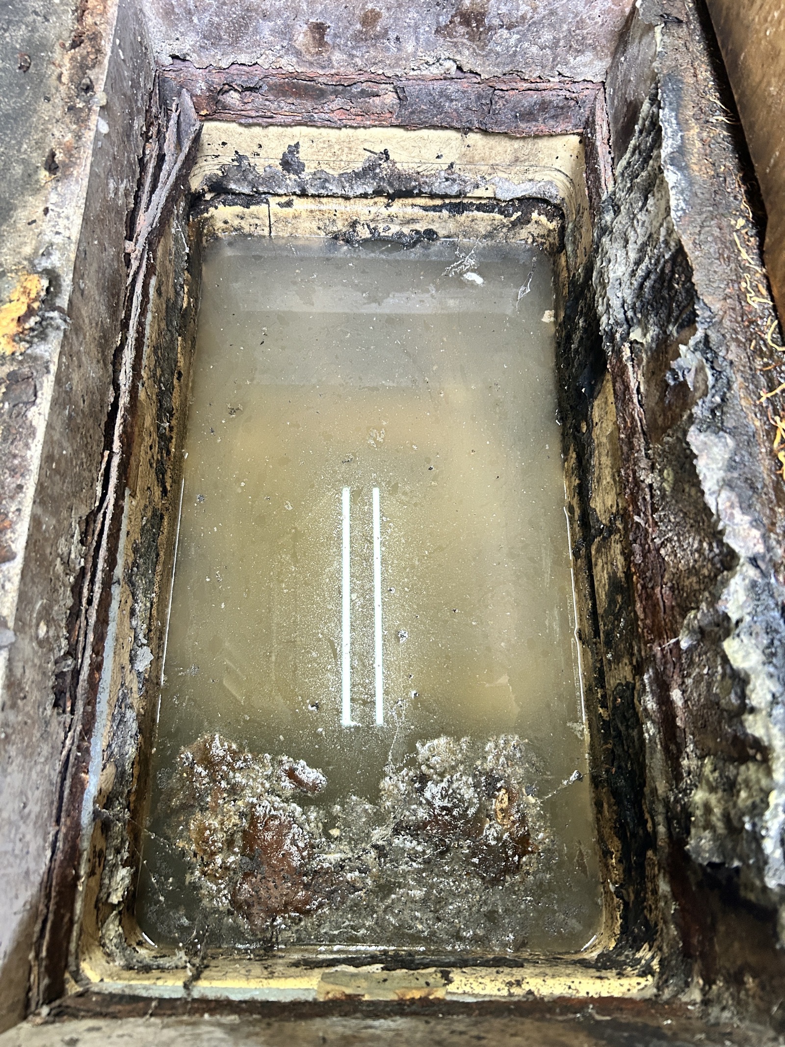 グリストラップ槽内の施工前状態。水面が濁り、槽壁には長期蓄積した油脂が固着している