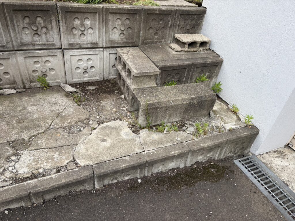 コンクリートブロック階段まわりのひび割れと雑草の侵食状況。目地に根が入り込んでいる