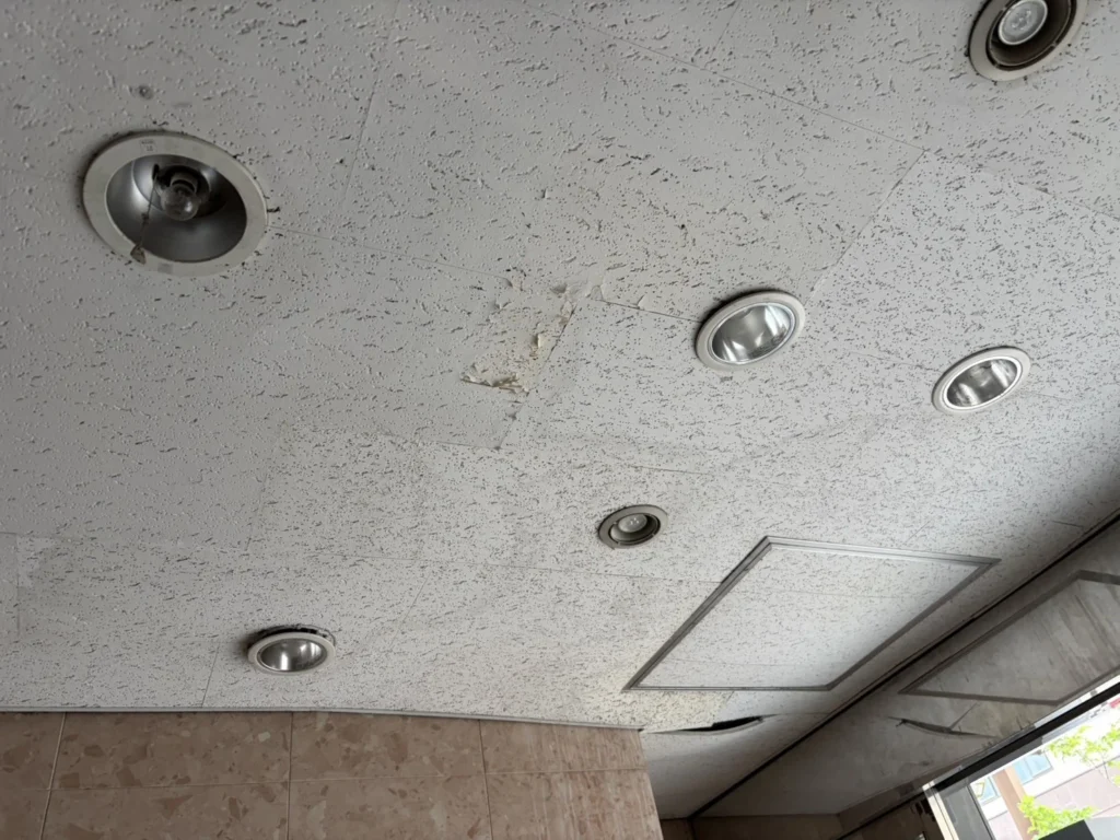 張り替え前の商業ビル天井。ダウンライト周りの変色と、ソーラトンの剥がれ・破れが目立つ共用部(札幌)