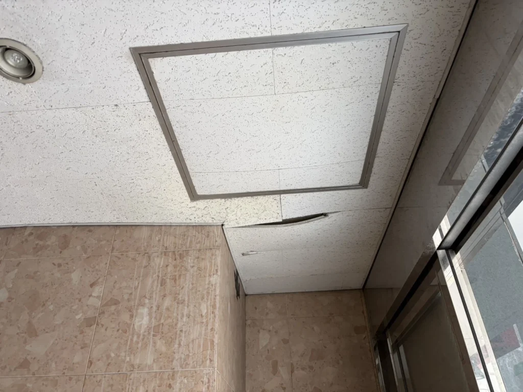 札幌市中央区の商業ビル共用部、張り替え前の天井。つぎはぎ状態のソーラトンと点検口、破損して穴があいた天井材