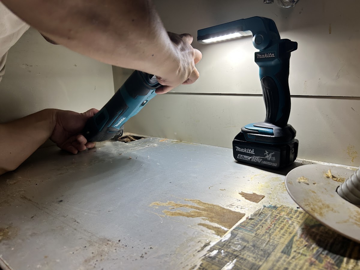 充電式ワークライトと工具を使ってシンク下の排水管を作業する様子