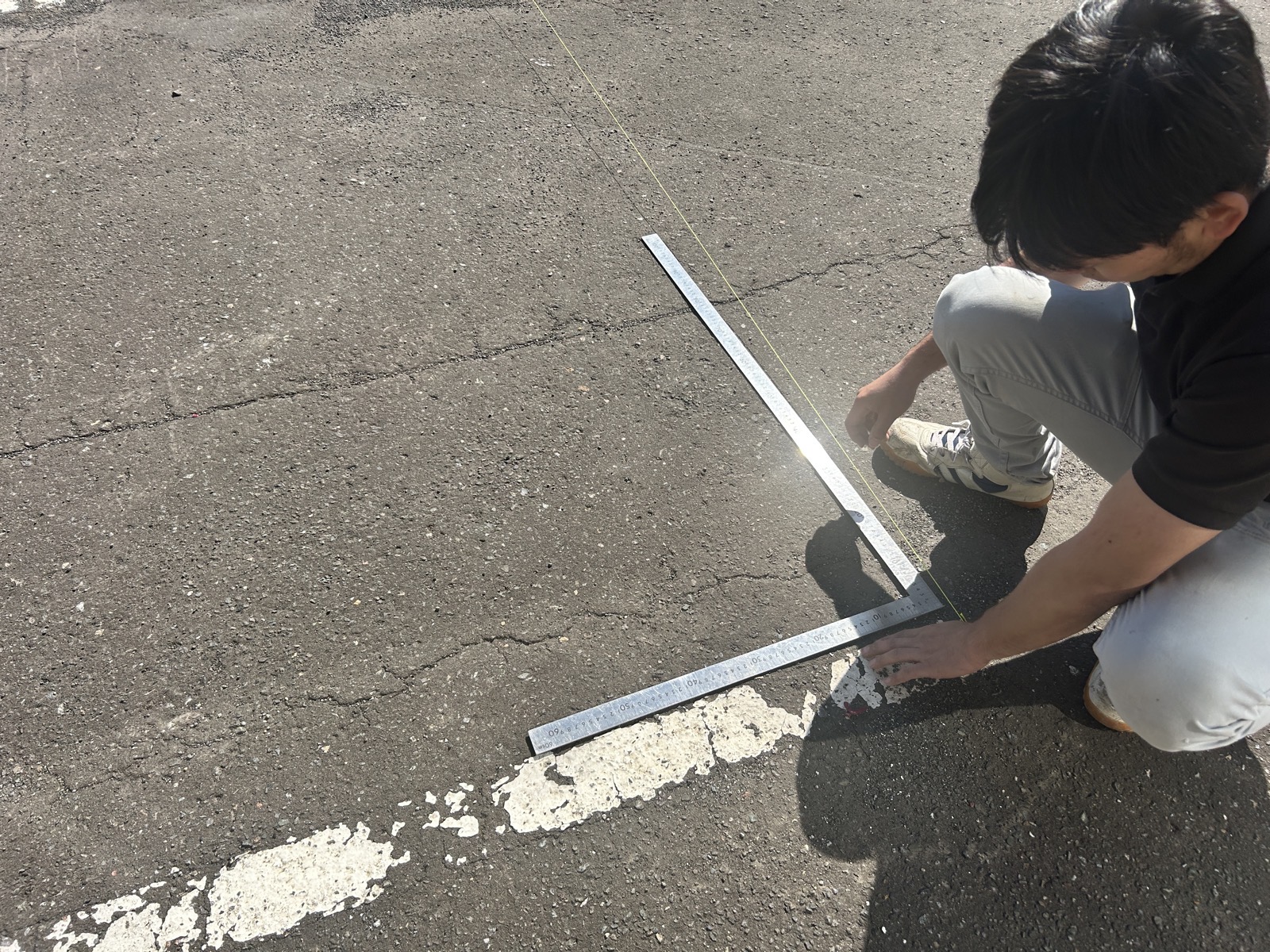 白線を基準に車止めの設置ラインを細かく測定している場面