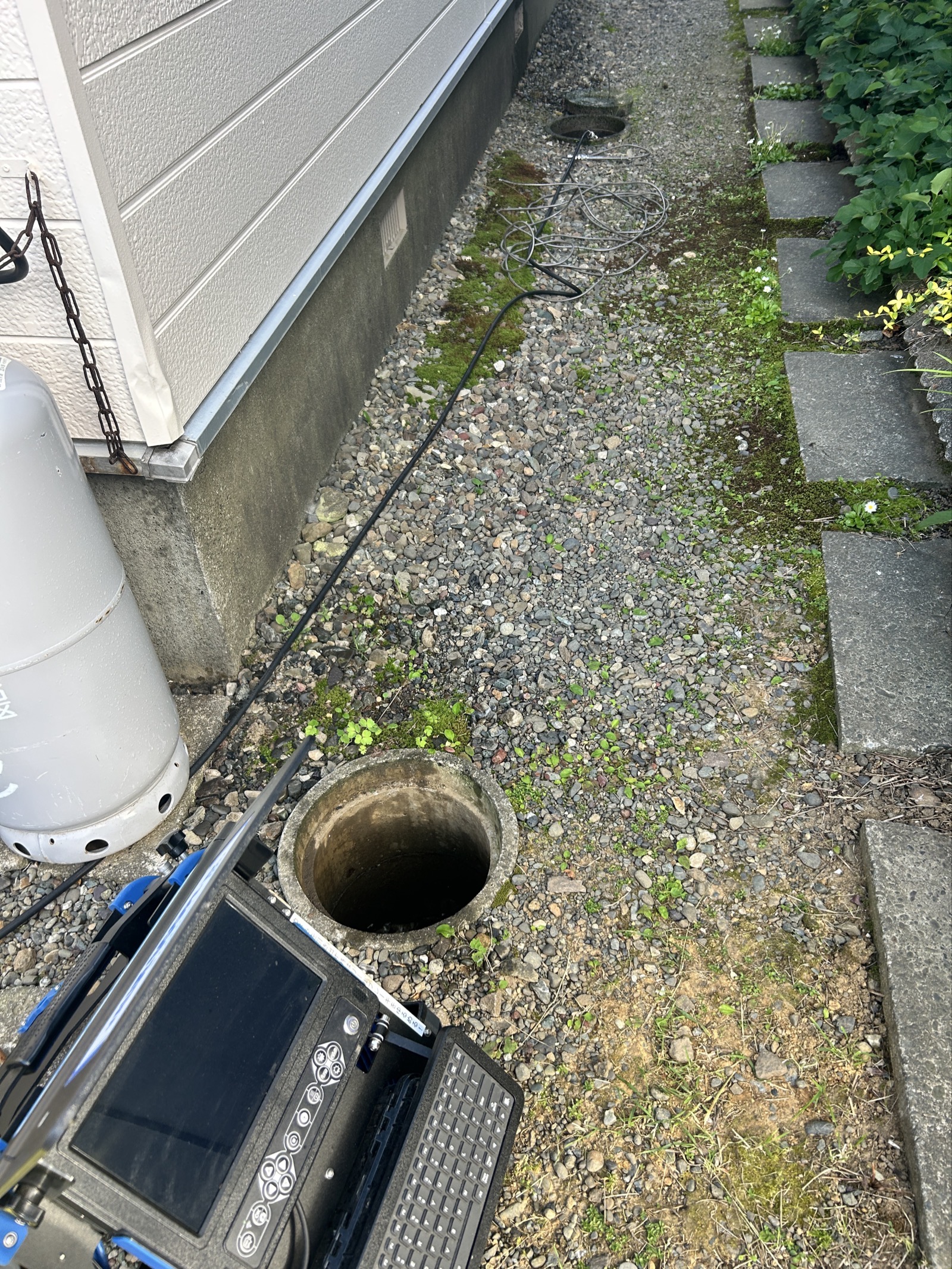 戸建て外壁沿いの排水マスに管内カメラのケーブルを挿入し調査する様子