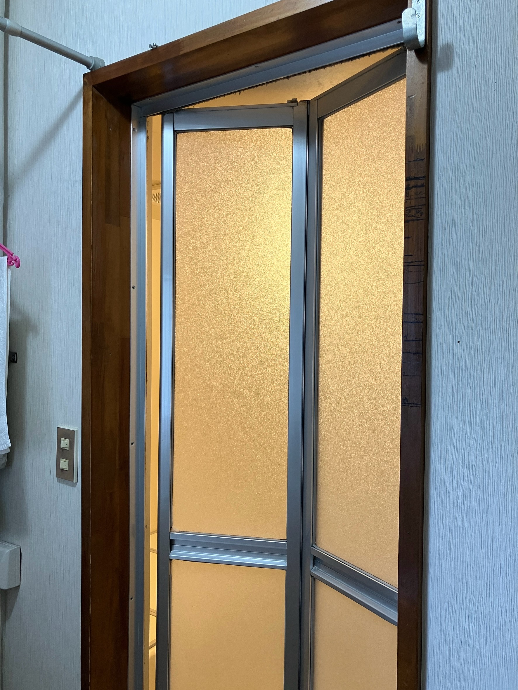交換前の浴室折戸を開けた状態。木製枠とアルミ框の折戸がすでに傷んでいます。