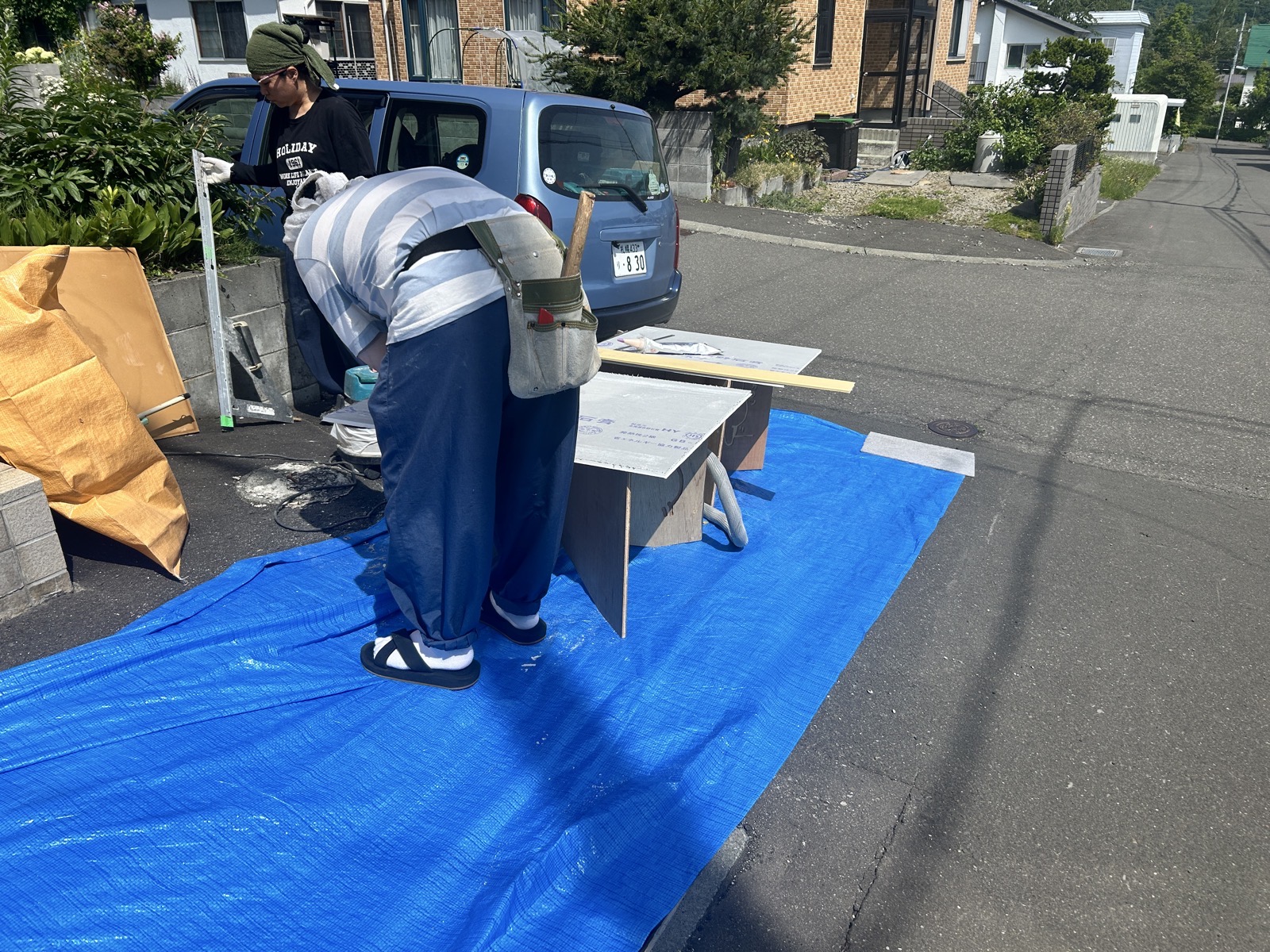 屋外のブルーシートの上で石膏ボードを採寸・カットする作業の様子