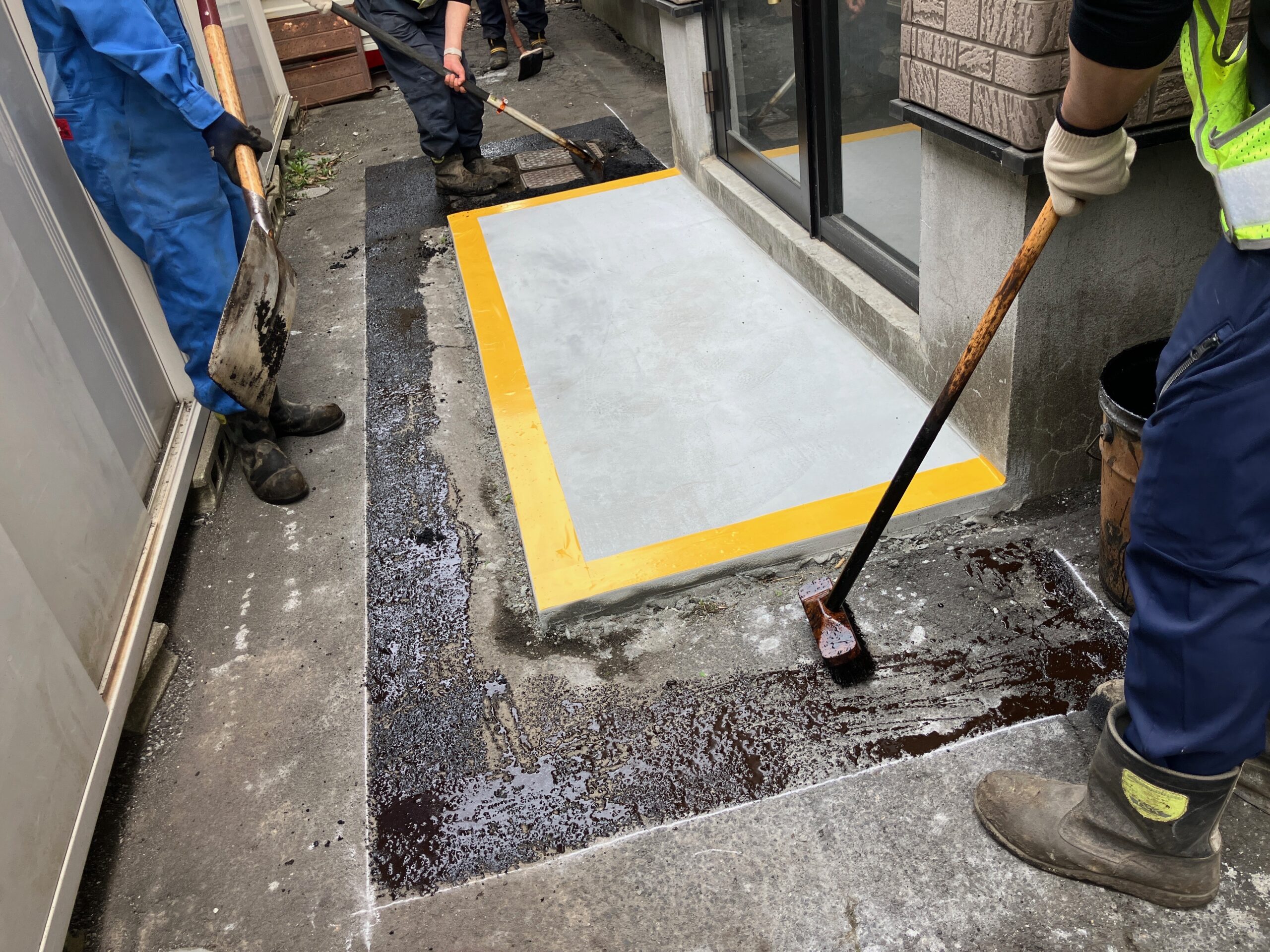 複数名の作業員によるアスファルト手均し作業の様子。狭い通路での施工