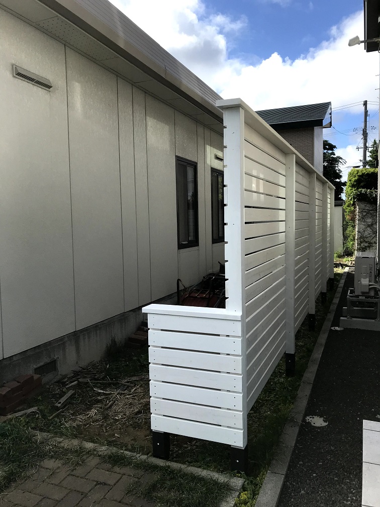 隣家との通路側から見た完成後の木製フェンス。柱は控えで支え、通路の明るさを保つ白色塗装で仕上げた