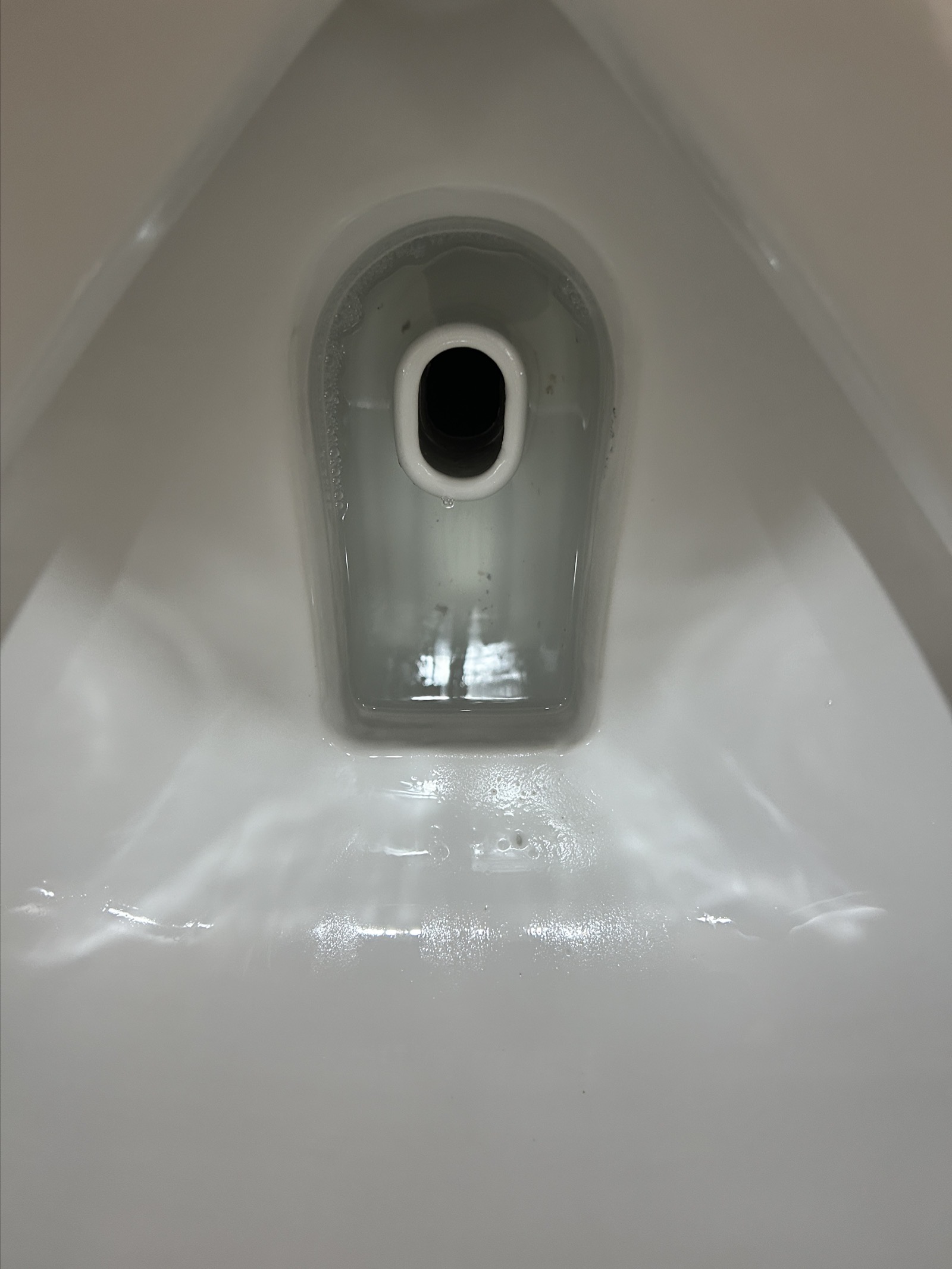 清掃後に復旧した小便器のトラップ部。封水が透明になった状態