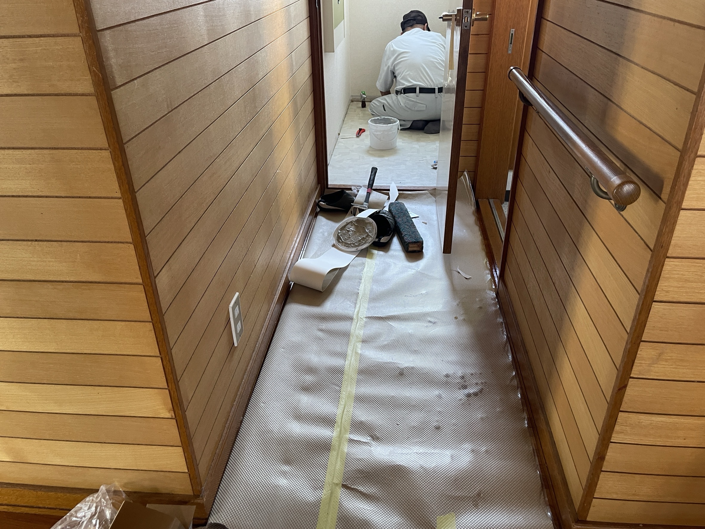 トイレ交換 費用に含まれる内装工事の様子。廊下奥でクロスを貼る職人