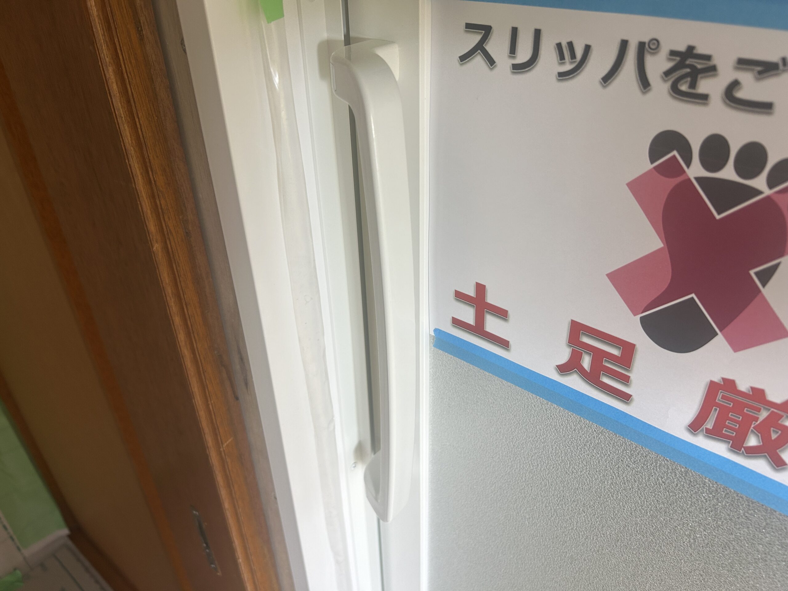 入口枠に付いた白い取っ手。扉のガラス面には土足厳禁の貼り紙がテープで留められている
