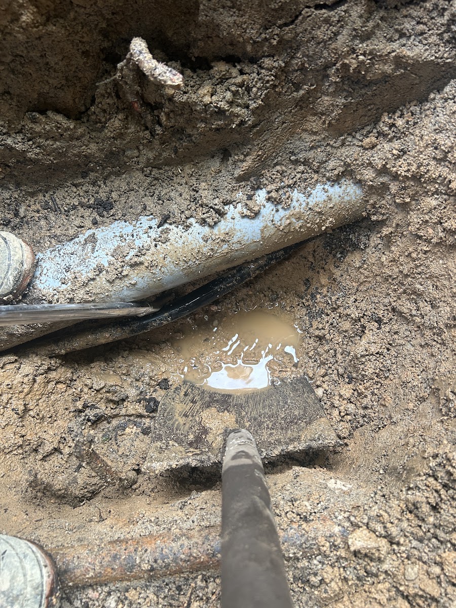 掘り進めた穴の中に見える水色の管と黒い管、底に溜まった泥水